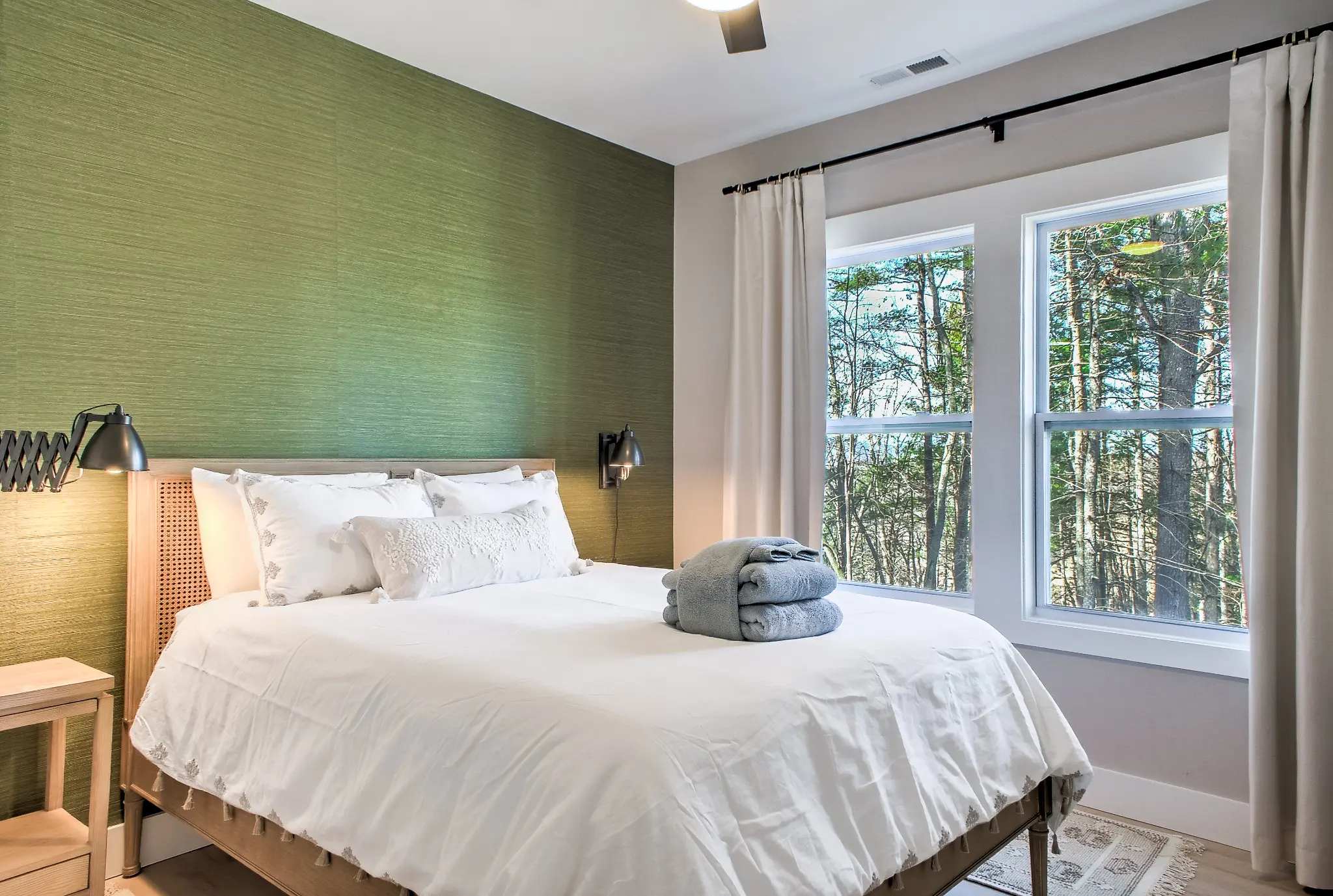 Queen guest bedroom with a soft green wall and windows overlooking the trees